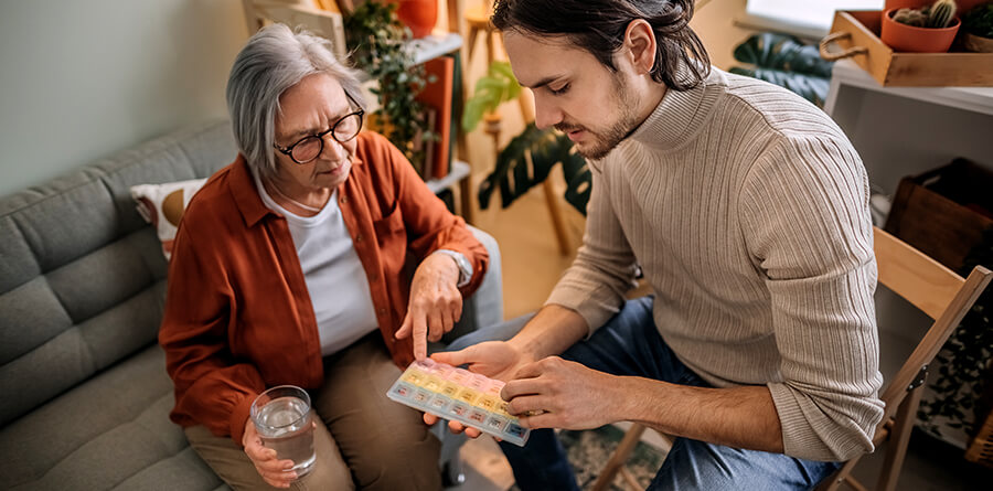 A caregiver helps educate an elderly patient with a pill box at home