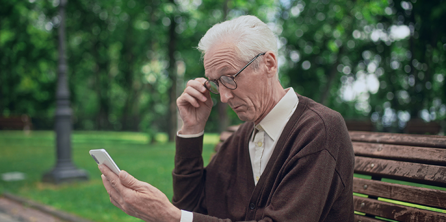 Elderly man reading news on smartphone through eyeglasses